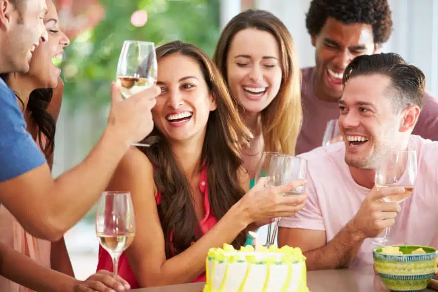 Group of friends celebrating birthday with cake and wine glasses