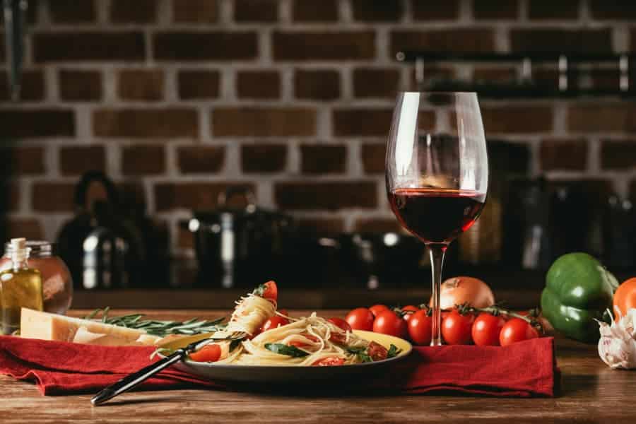Traditional Italian pasta with tomatoes and arugula in plate and glass of red wine